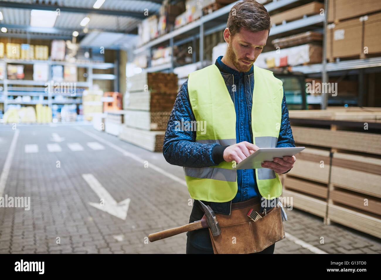 Jeune employé de l'entrepôt de fournitures de construction debout dans un lecteur à travers la consultation d'un ordinateur tablette de poche Banque D'Images