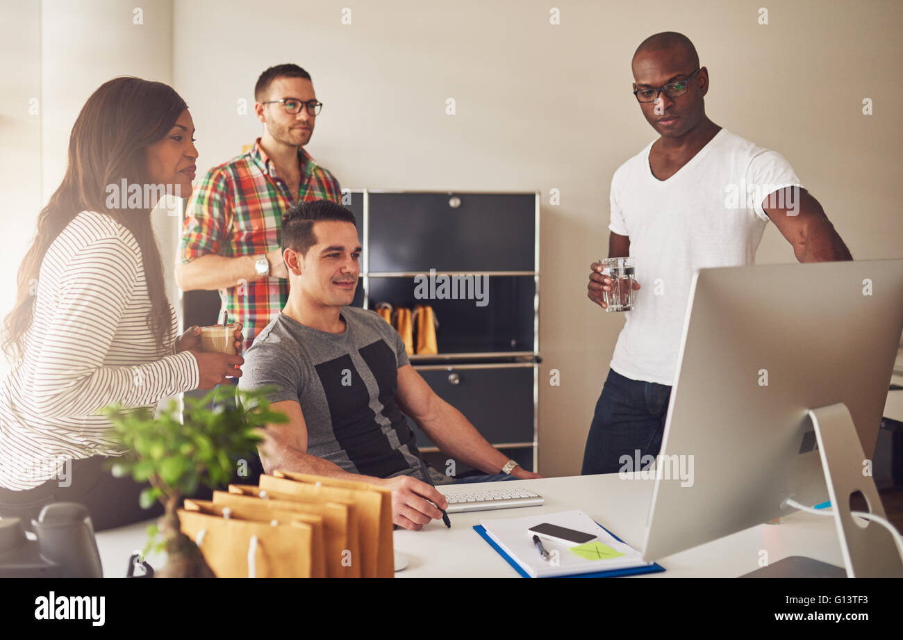 Groupe diversifié de jeunes adultes multi-ethnique des gens d'affaires réunis autour de 24 regarder quelque chose sur leur écran d'ordinateur Banque D'Images