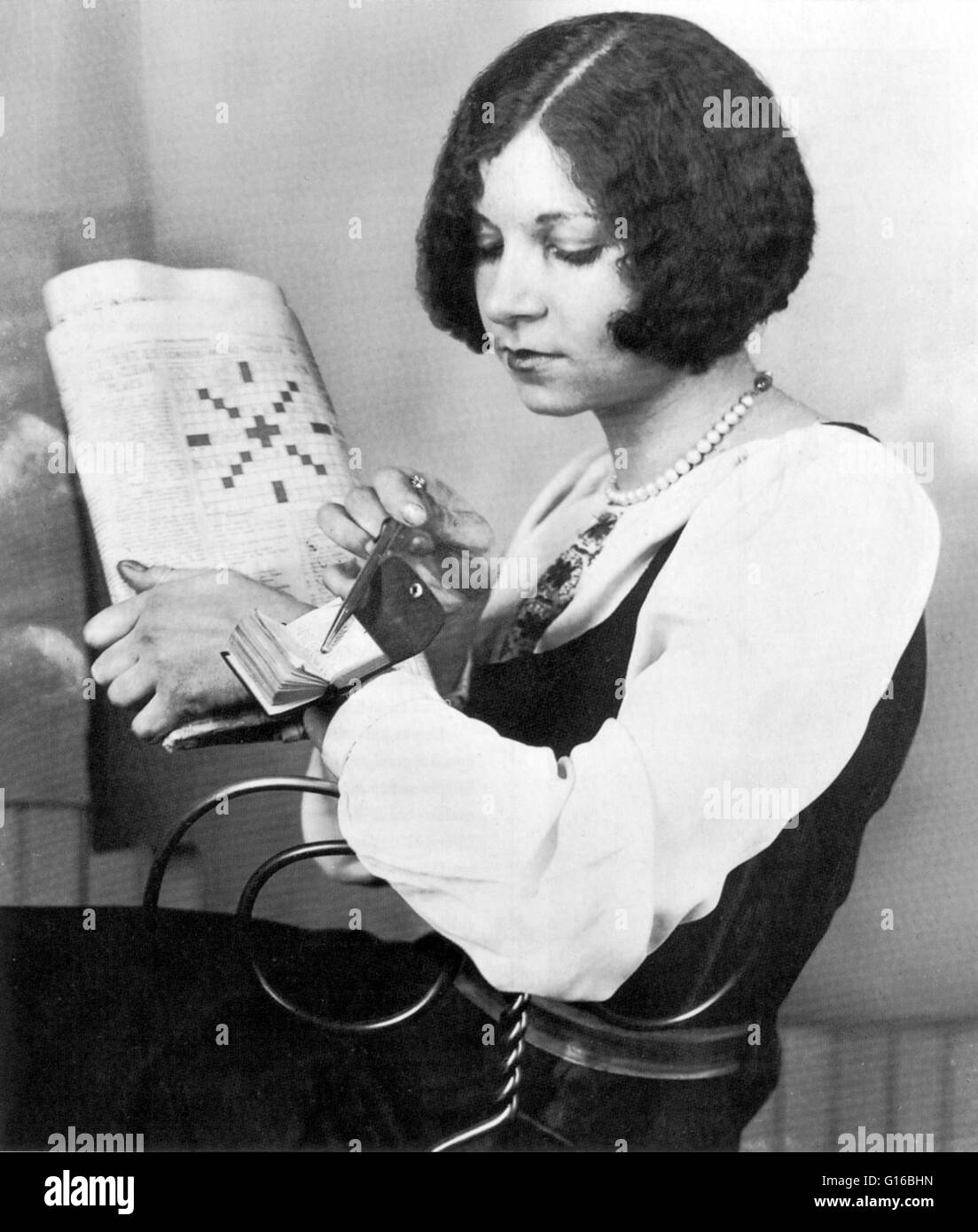 Les années 1920 a apporté un jeu de mots croisés à la mode aux États-Unis. Cette jeune femme regarde dieu solaire égyptien '' dans le plus petit du monde dictionnaire de mots croisés, attaché à son poignet. Un jeu de mots croisés est un puzzle qui prend habituellement la forme d'un carré o Banque D'Images