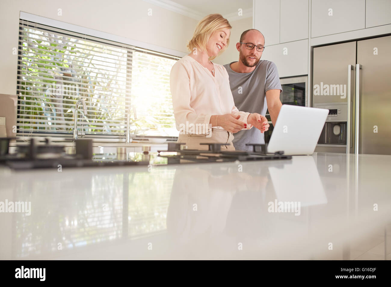 Tourné à l'intérieur d'un couple heureux à l'aide d'un ordinateur portable dans la cuisine. Femme montrant quelque chose sur l'ordinateur portable à l'homme. Banque D'Images