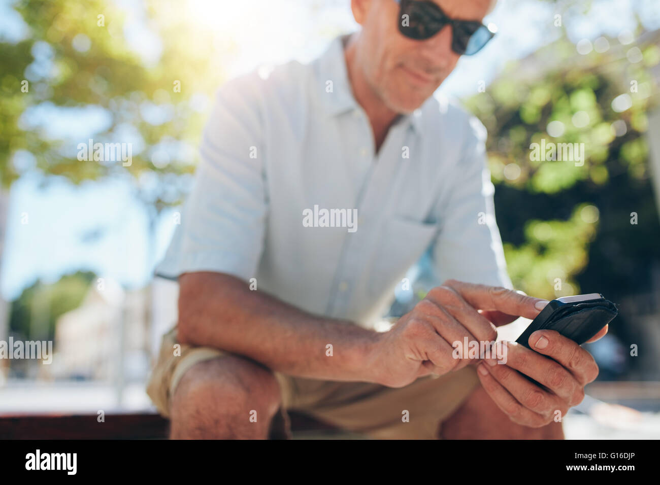 Close up portrait of senior man using cell phone, assis sur un banc dans la ville sur une journée ensoleillée. L'accent sur mains tenant mob Banque D'Images