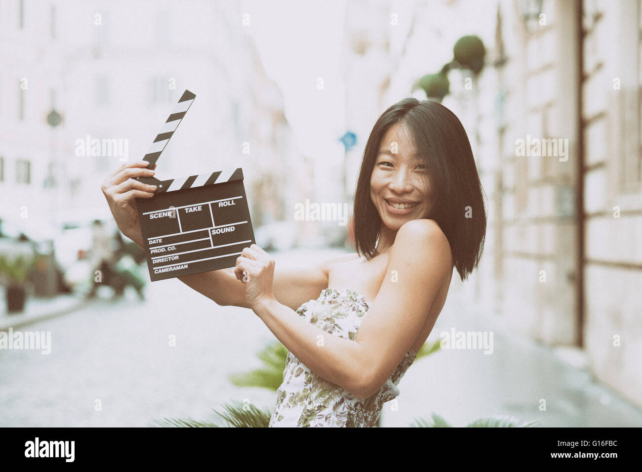 Young Asian woman smiling et montrant clapper board sur la rue printemps dress Banque D'Images