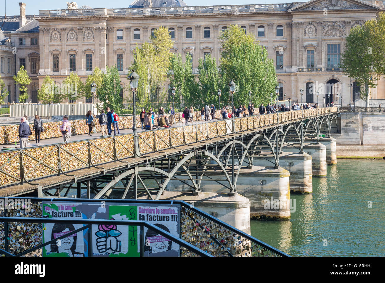 Les piétons traversent la Seine à Paris sur le Pont des Arts, c'est forgé recouvert de cadenas. Musée du Louvre en arrière-plan. Banque D'Images