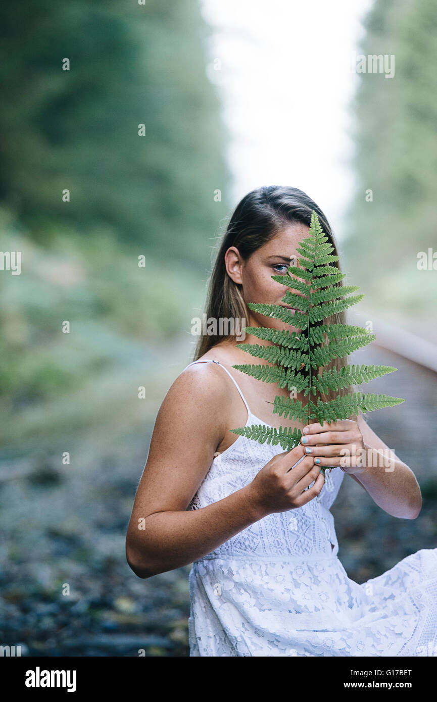 Adolescente, assis à l'extérieur, holding plant in front of face Banque D'Images