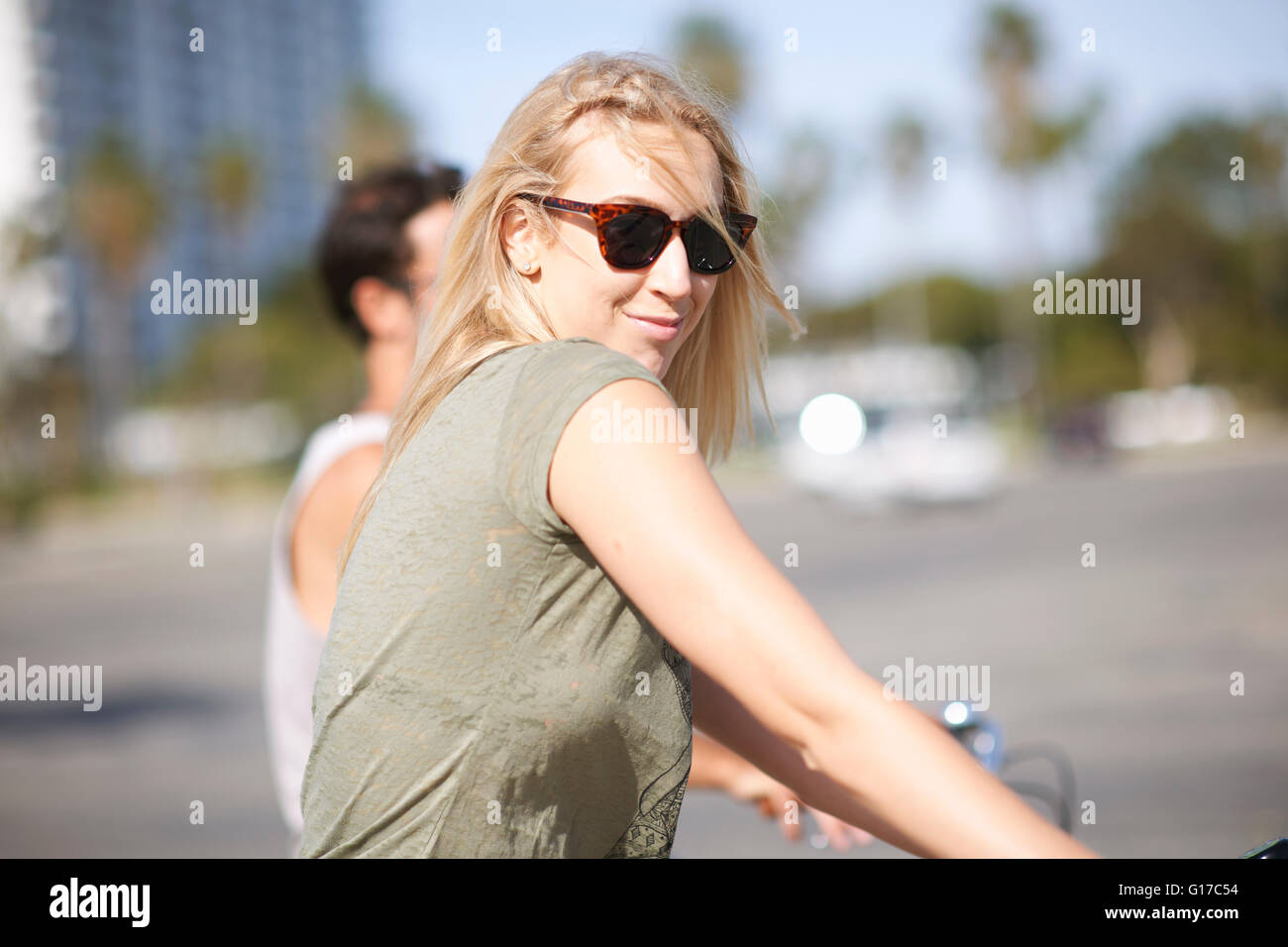 Jeune femme à la Par-dessus son épaule tandis que le vélo avec copain à Venice Beach, Los Angeles, Californie, USA Banque D'Images
