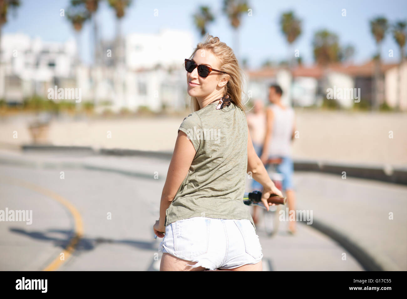 Jeune femme à la recherche de cyclistes par-dessus son épaule tandis que le vélo à Venice Beach, Los Angeles, Californie, USA Banque D'Images