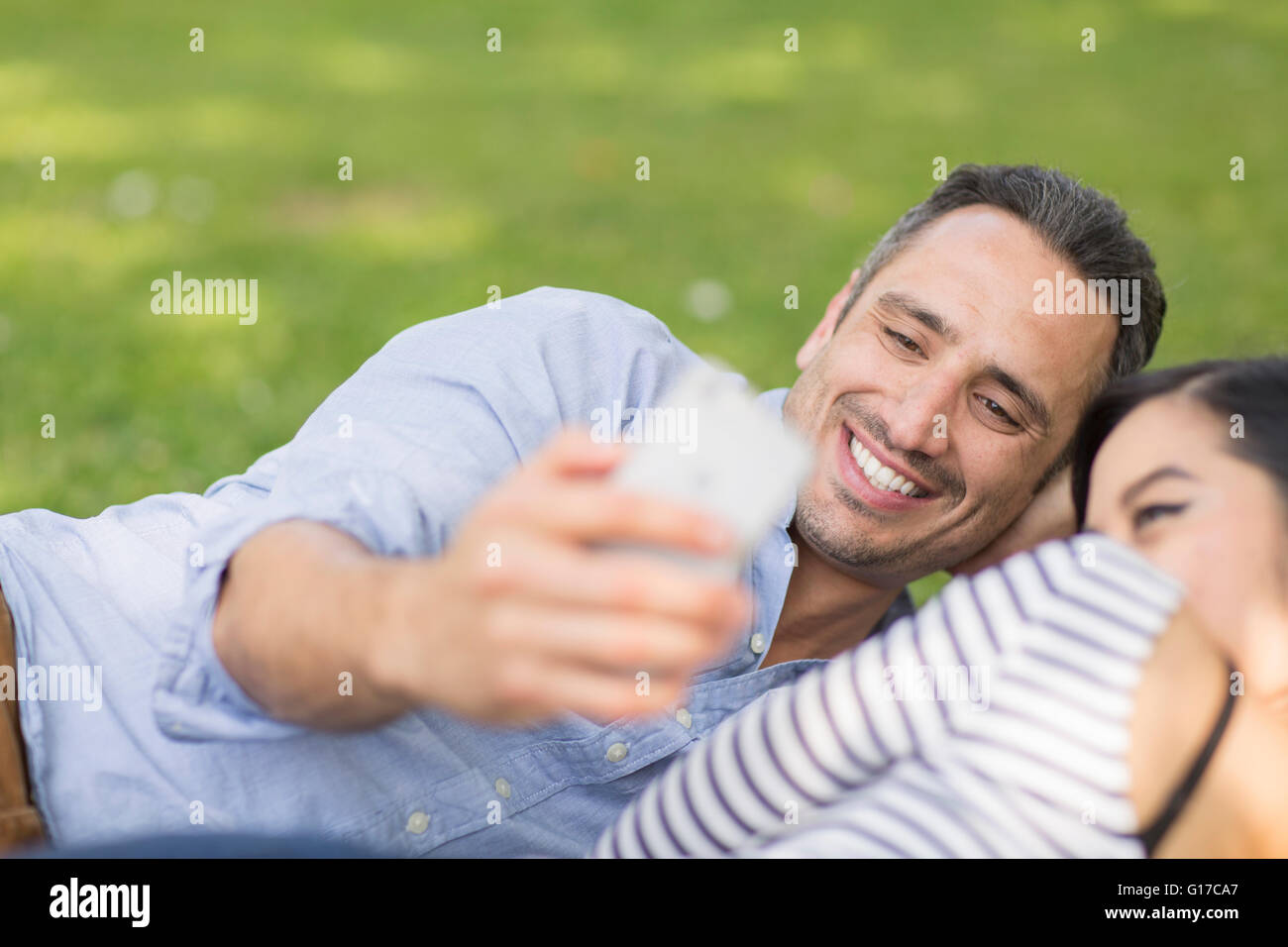 Couple lying on grass using smartphone pour prendre des selfies Banque D'Images