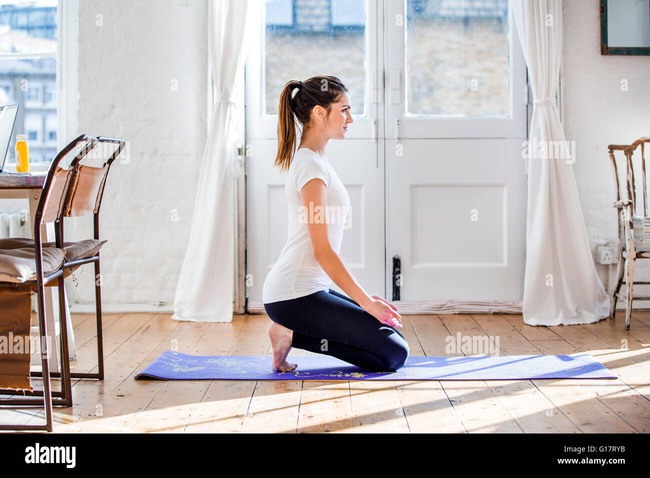 Young woman practicing yoga position agenouillée dans l'appartement Banque D'Images