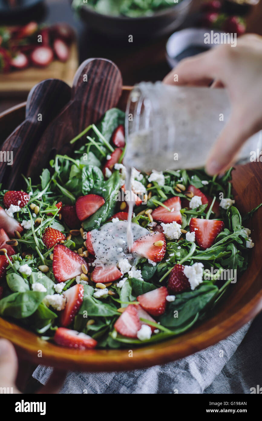 Une femme est photographié en versant vinaigrette aux graines de pavot dans une fraise et salade d'épinards. Banque D'Images