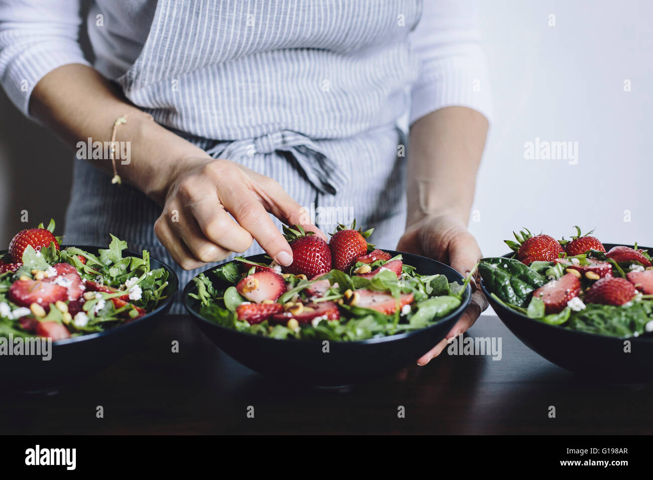 Une femme est photographié à partir de la vue de face, tout en plaçant une fraise dans un bol d'épinards et de fraises salade de roquette. Banque D'Images