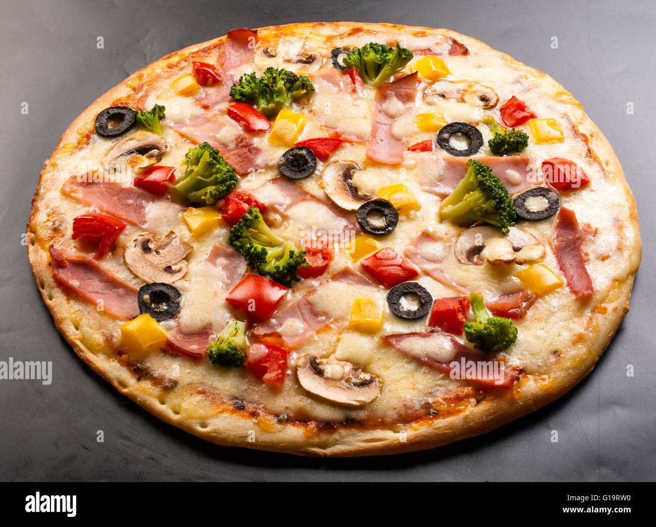 La pizza sur un fond sombre avec du jambon, champignons, chou-fleur, olives, fromage et piment doux Banque D'Images