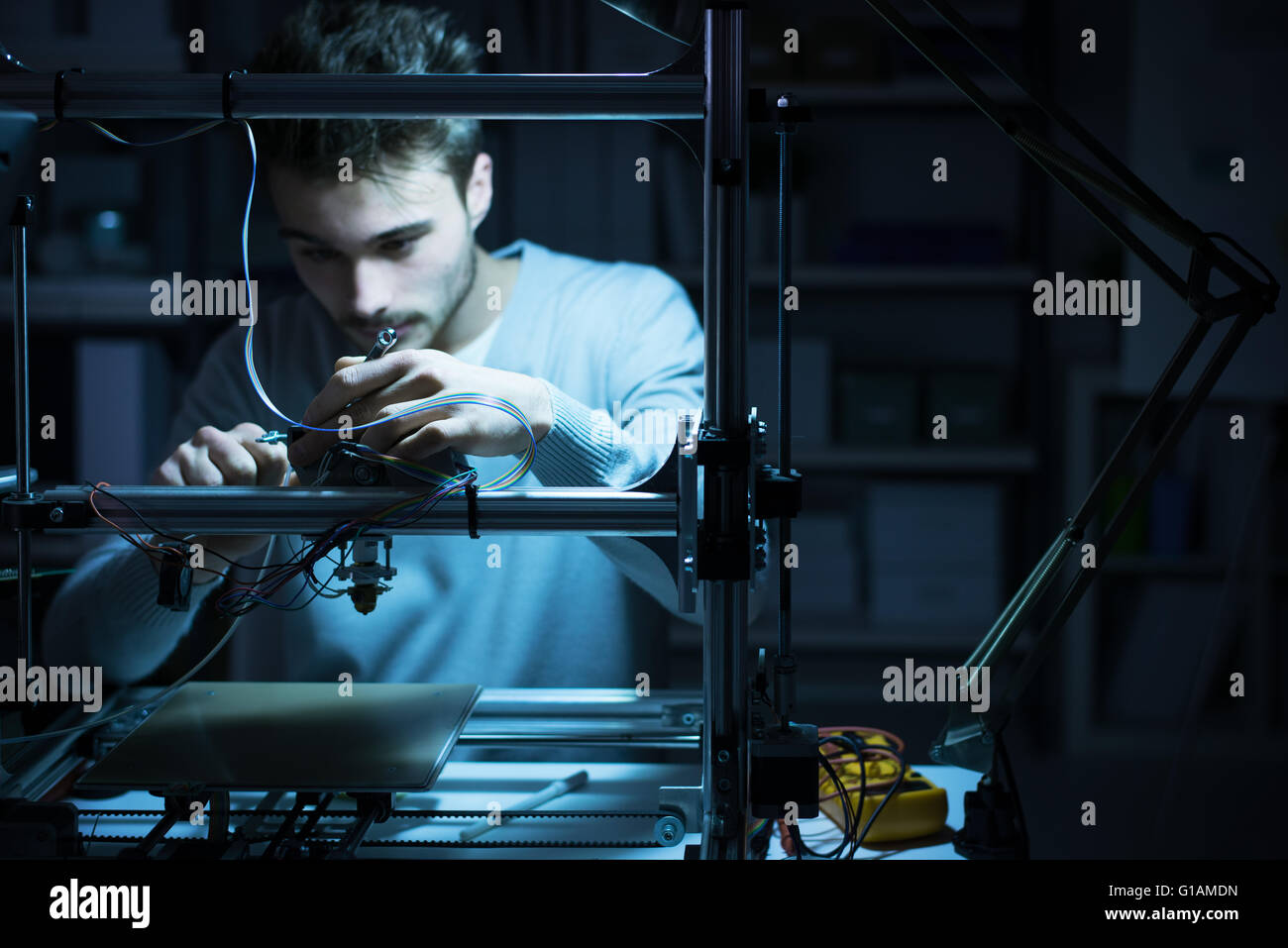 Jeune ingénieur travaillant de nuit dans le laboratoire, il est l'ajustement d'un des composants de l'imprimante 3D, la technologie et l'ingénierie concept Banque D'Images