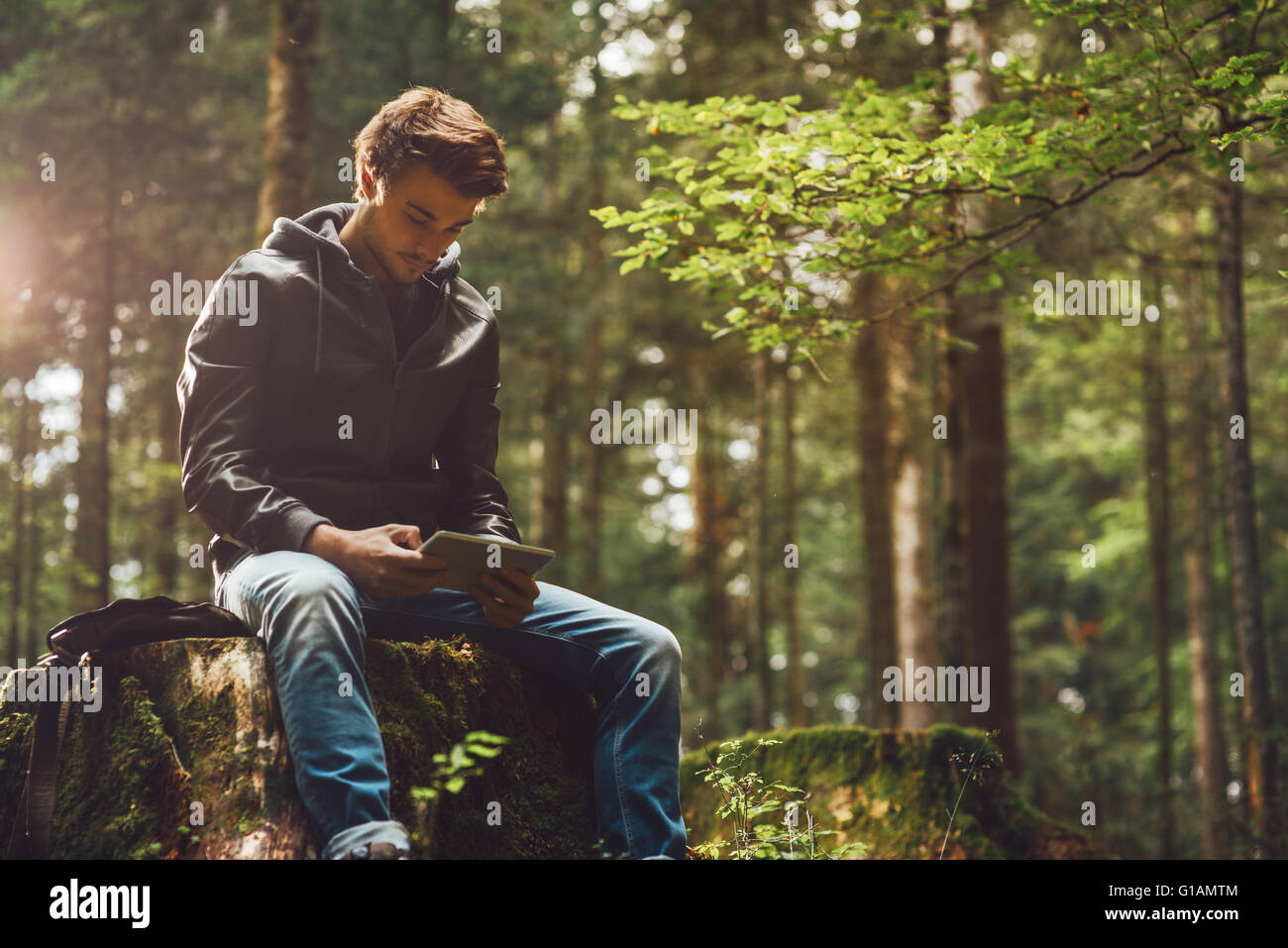 Beau jeune homme assis dans les bois et à l'aide d'un écran tactile numérique, connexion wi-fi et la liberté concept Banque D'Images