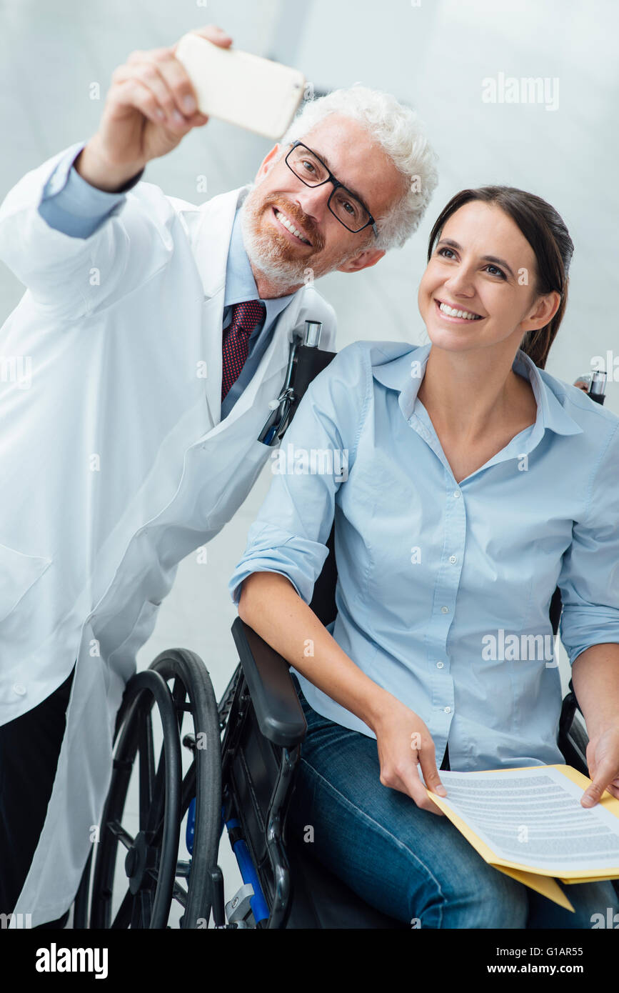 Smilng médecin prenant autoportraits avec un patient en fauteuil roulant à l'aide d'un téléphone intelligent, de soins et de l'invalidité du concept d'intégration Banque D'Images