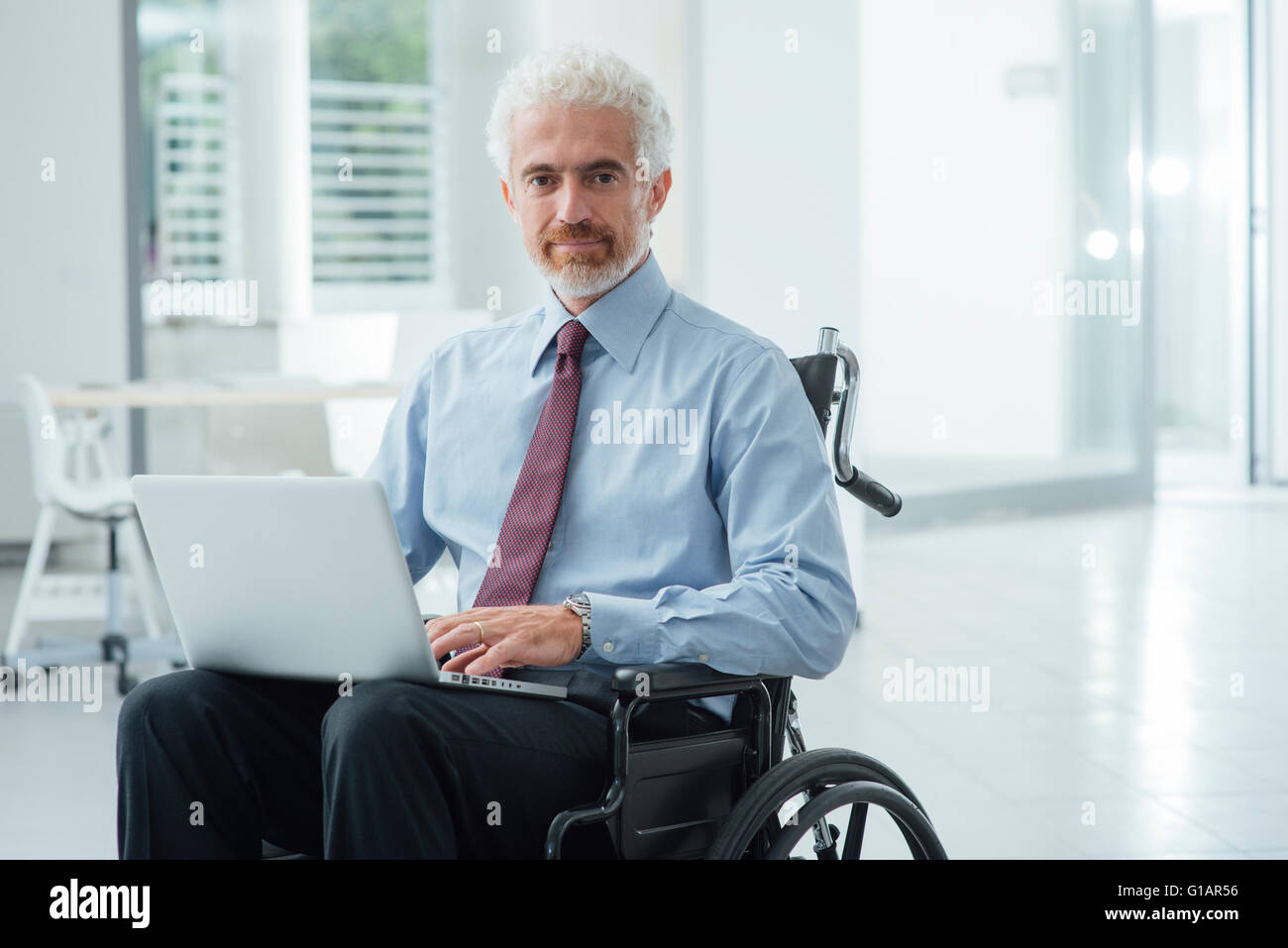 Homme d'entreprise réussie en fauteuil roulant à l'aide d'un bureau de travail et ordinateur portable Banque D'Images