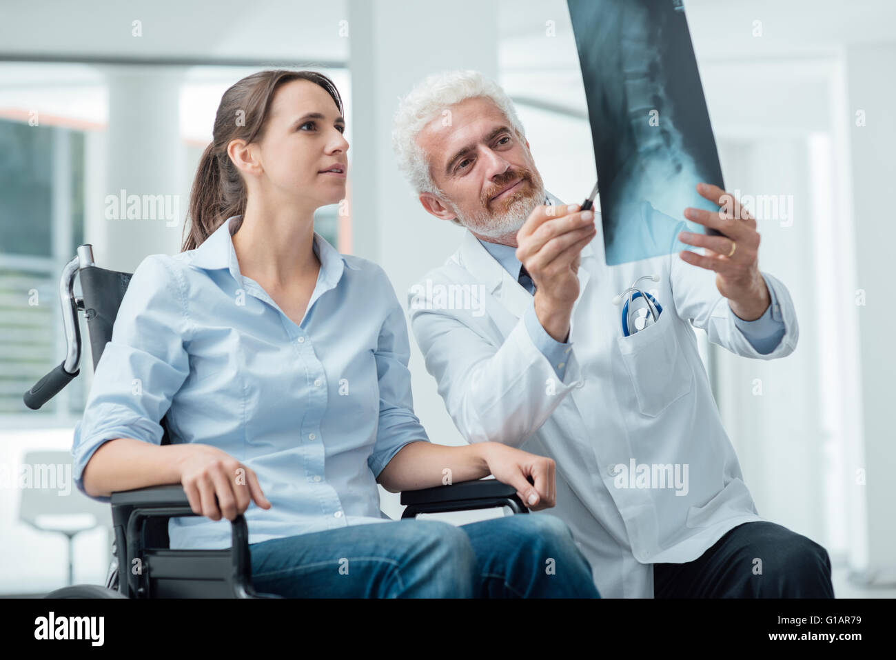 Le radiologue examinant une femme en fauteuil roulant's x-ray de colonne vertébrale humaine lors d'une visite à l'hôpital Banque D'Images