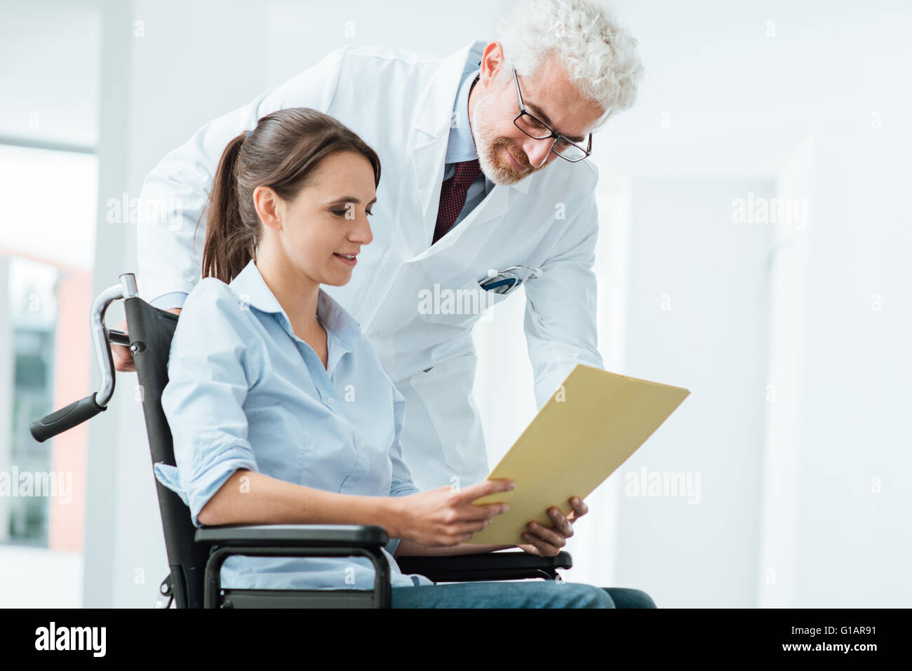 Médecin et patient de l'examen d'un fichier avec des dossiers médicaux, elle est assise sur un fauteuil roulant, d'assistance et de soins de santé concept Banque D'Images