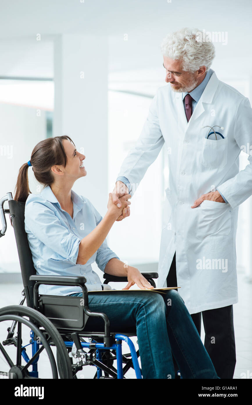 Confiant smiling doctor shaking hands with his new patient, elle est une jeune femme en fauteuil roulant Banque D'Images