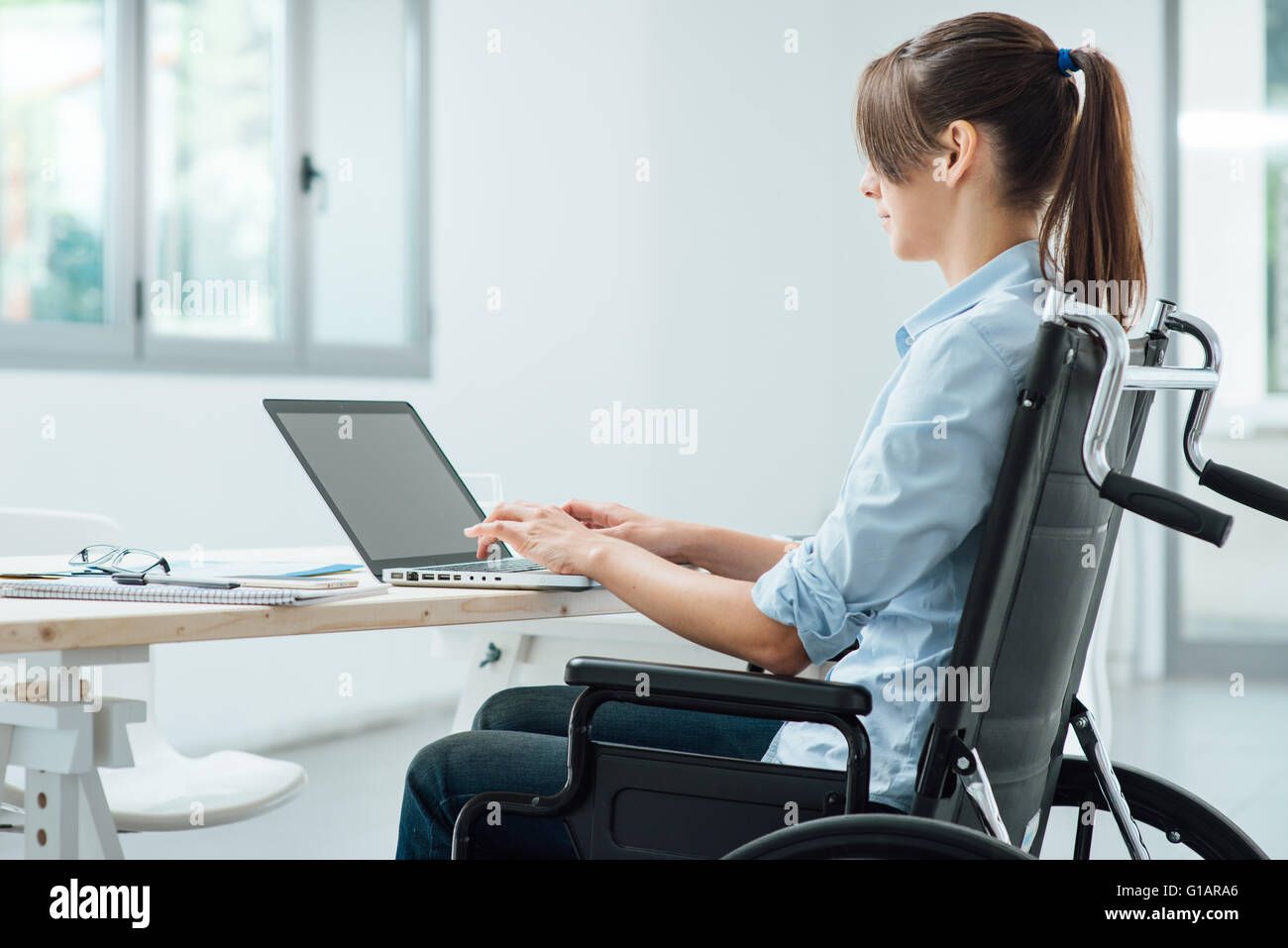 Les jeunes personnes handicapées business woman in wheelchair travaillant au bureau et la saisie sur un ordinateur portable, l'accessibilité et l'indépendance concep Banque D'Images