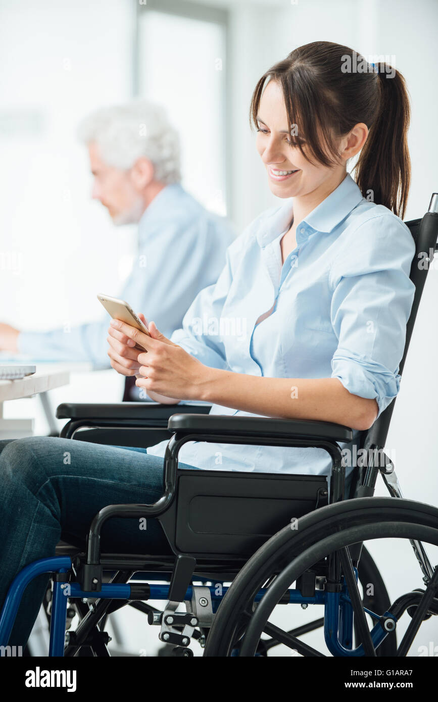 Business Woman in wheelchair travaillant au bureau et des textos avec son téléphone mobile, l'invalidité et l'emploi d'hiver Banque D'Images