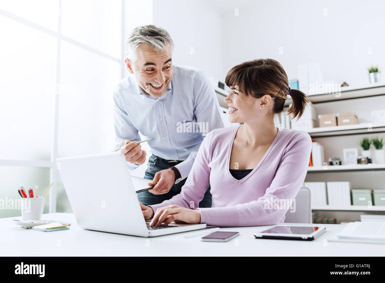 Cheerful des gens d'affaires de l'office, ils travaillent ensemble et souriant, la femme est la saisie sur un ordinateur portable Banque D'Images