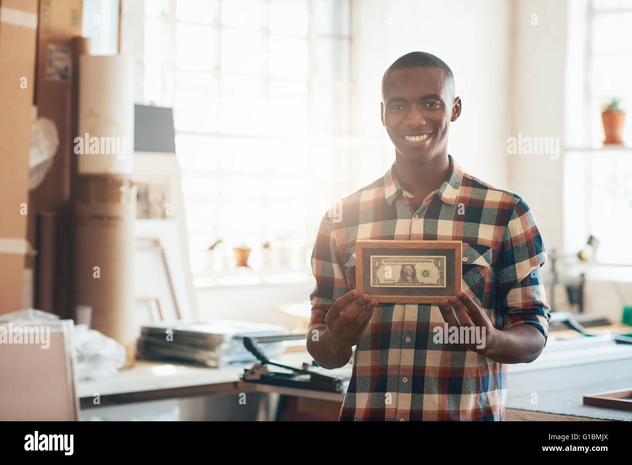 Portrait d'un jeune entrepreneur africain fier smiling at the camera and holding a pans dollar bill, qui est la première de l'argent Banque D'Images