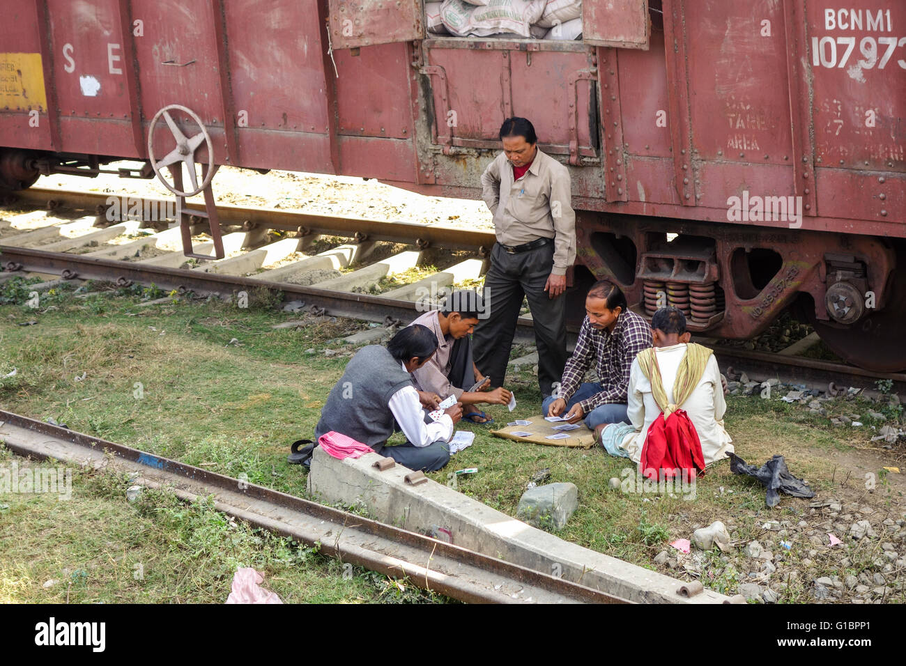 Quatre hommes passent du temps en jouant à un jeu de cartes assis en plus de voie de chemin de fer dans l'ouest du Bengale, en Inde Banque D'Images