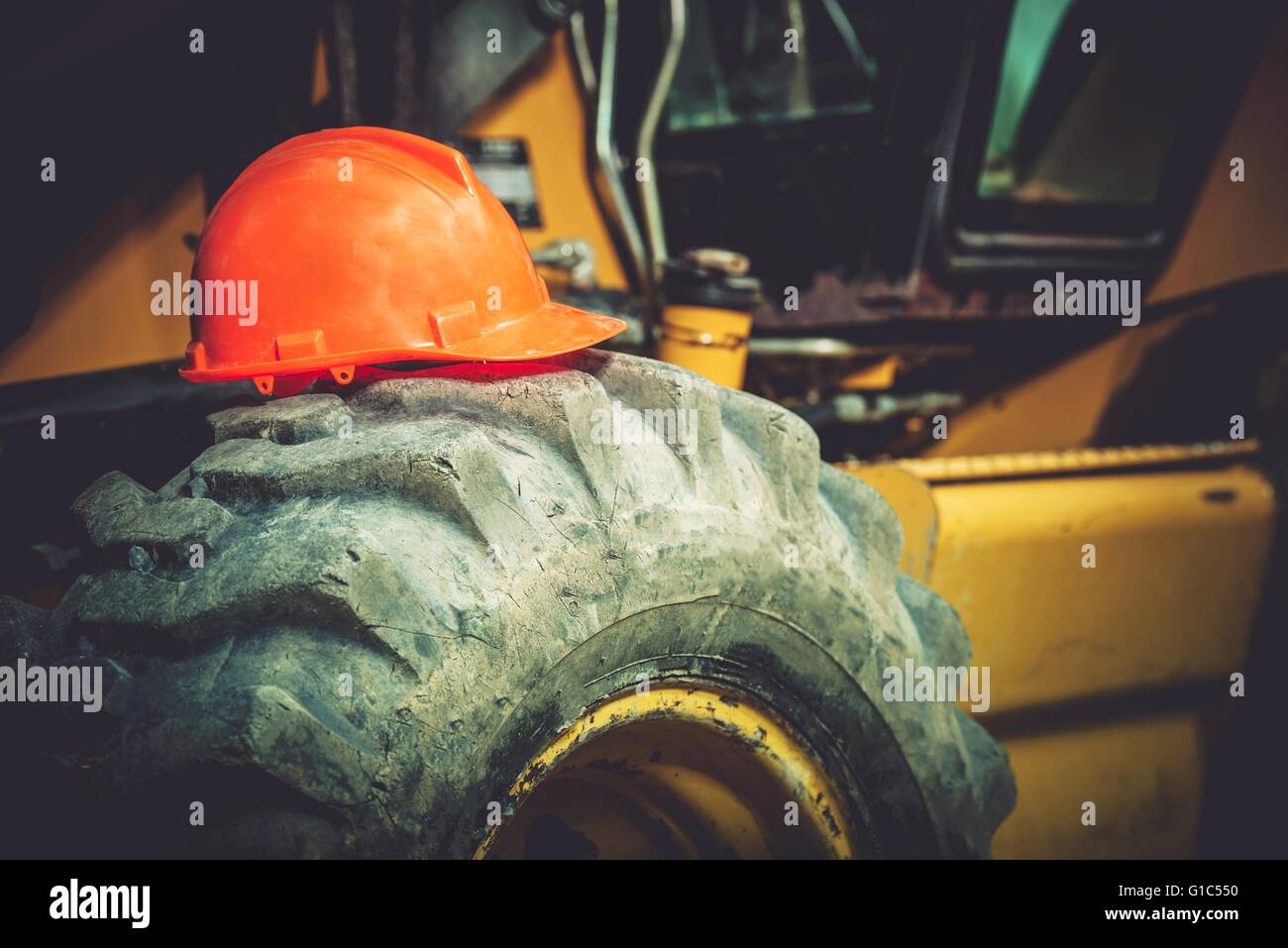 Concept de sécurité au travail. Pendant que la construction de la sécurité au travail. Casque de sécurité de construction orange sur de gros Heavy Duty pneu du tracteur. Banque D'Images