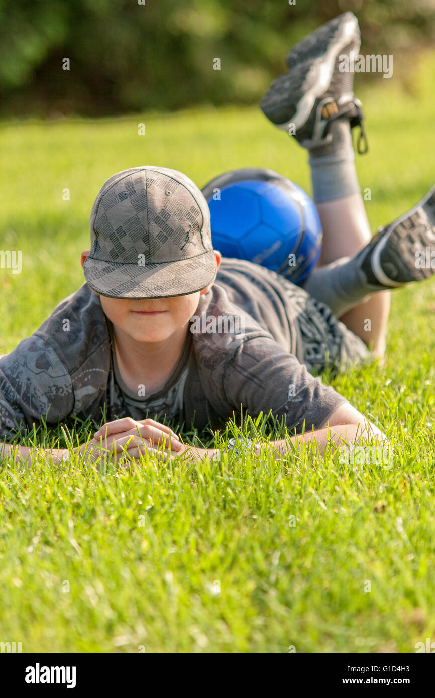 Jeune garçon portant sur l'herbe, les jambes et un ballon de soccer sur ses jambes. Banque D'Images