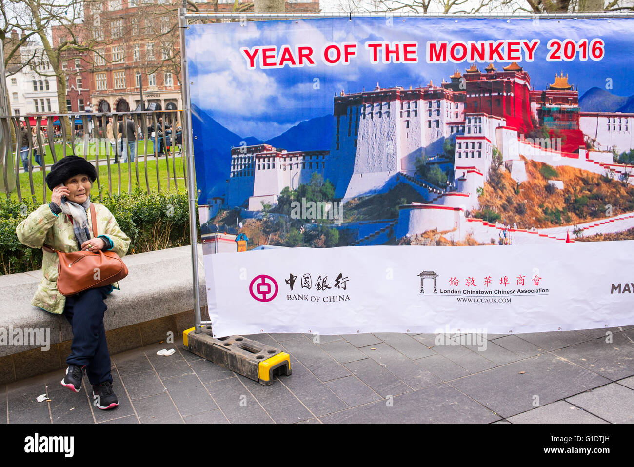 Grand panneau célébrant le nouvel an chinois 2016, "Année du singe' avec l'ancienne femme chinoise au téléphone assis près d'elle. Banque D'Images