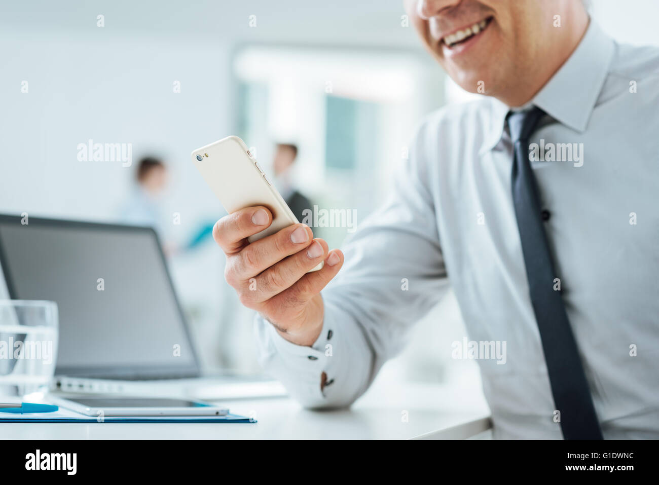Businessman sitting at office desk en utilisant un écran tactile smart phone, les mains de près, l'intérieur du bureau et les gens d'affaires à l'arrière Banque D'Images