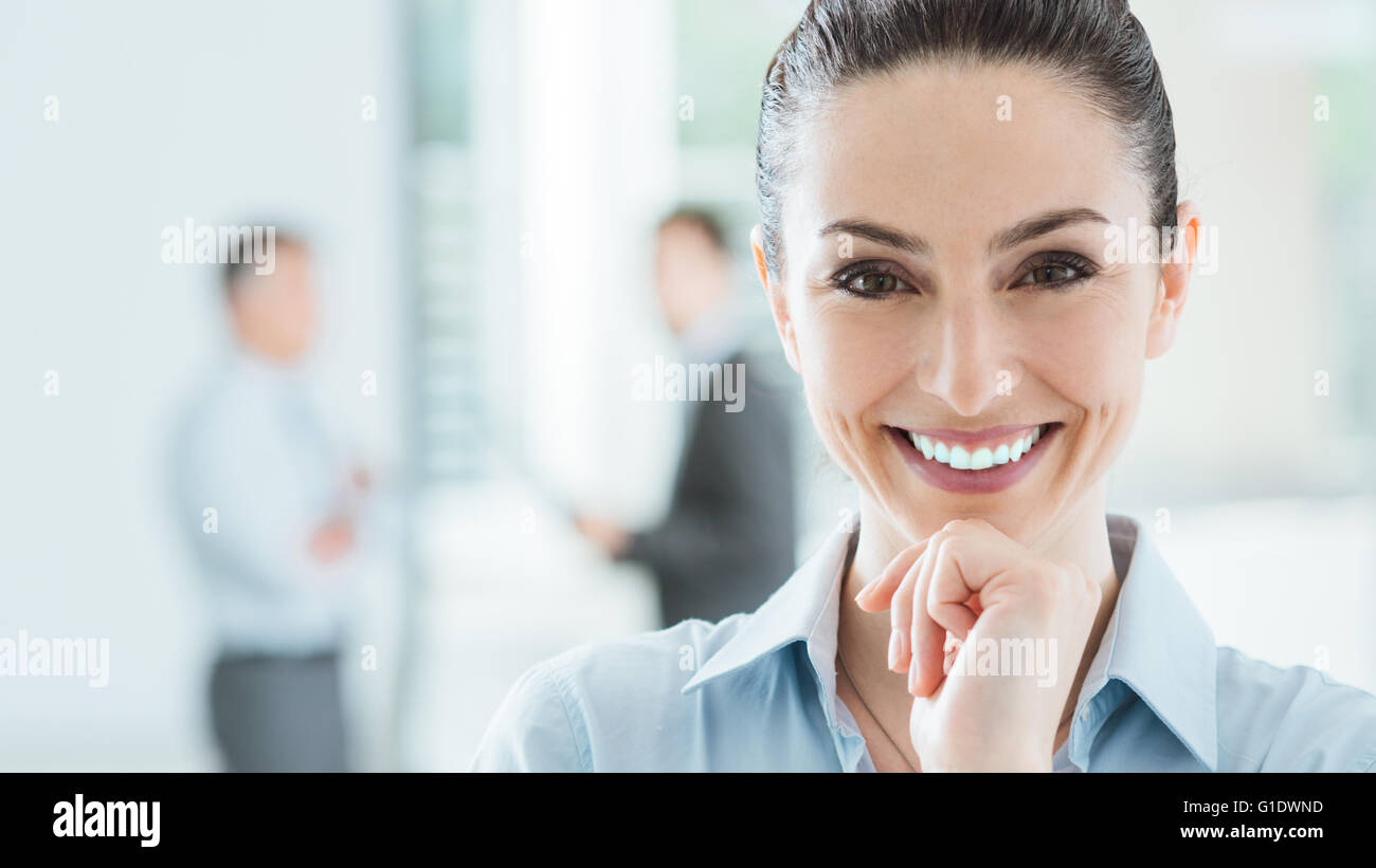 Confiant beautiful smiling business woman dans le bureau posing with hand on chin et looking at camera, office interior et bus Banque D'Images