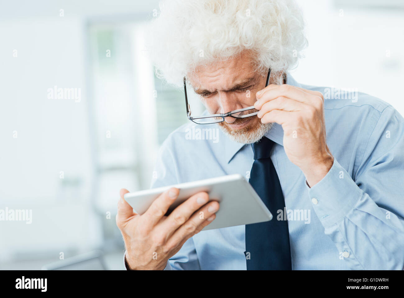 Businessman ayant des problèmes de vue, il est à l'aide d'une tablette et réglage de ses lunettes, l'arrière-plan sur l'intérieur de bureau Banque D'Images