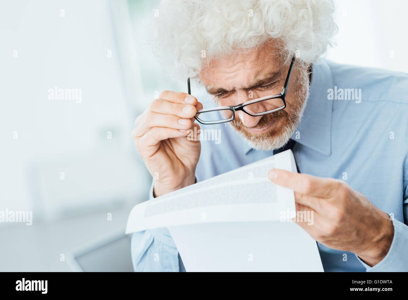 Employé de bureau de mâles adultes ayant des problèmes de vue lors de la lecture de la paperasse avec petit texte Banque D'Images