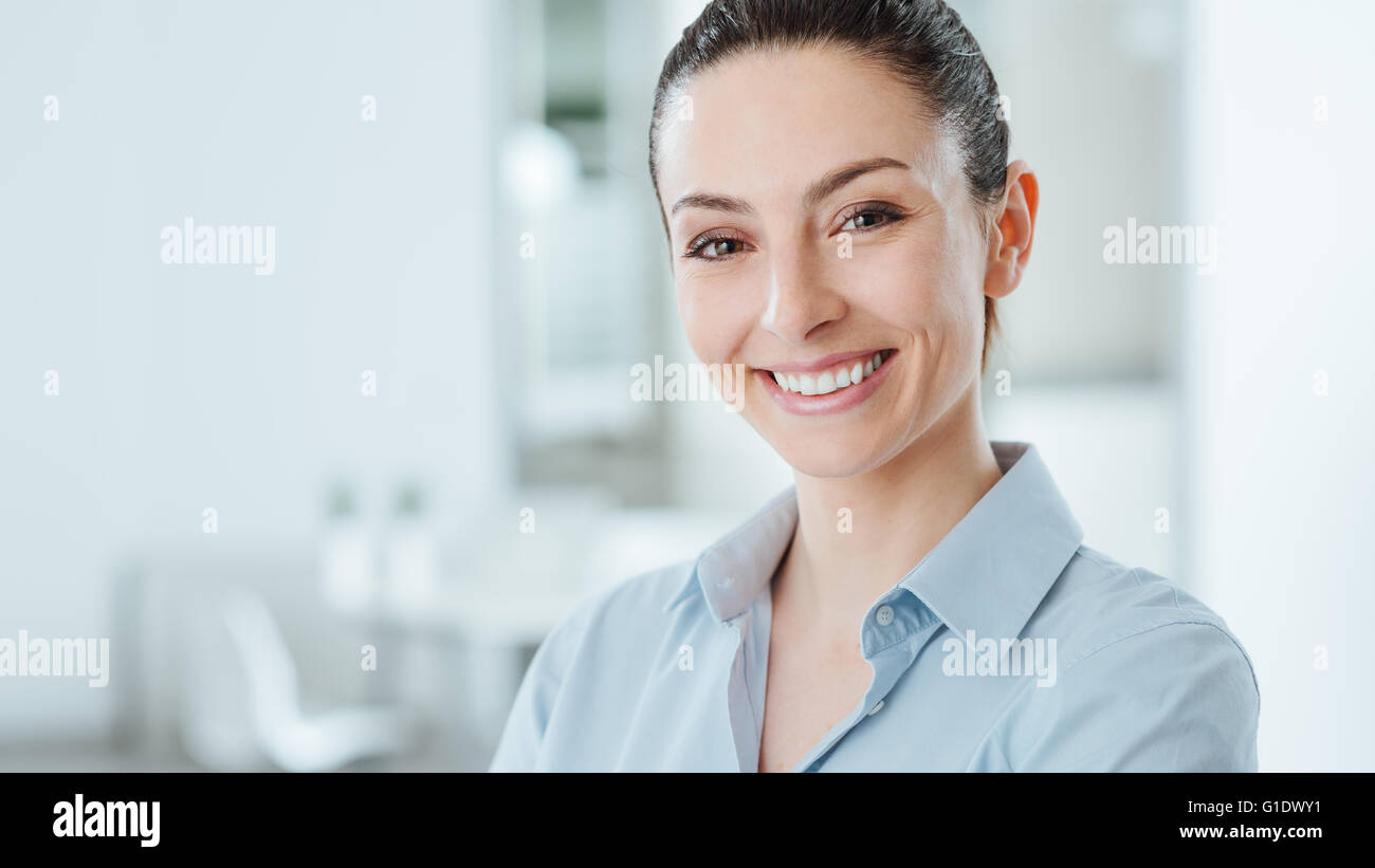Beau confident business woman posing and smiling at camera, cabinet intérieur sur l'arrière-plan Banque D'Images