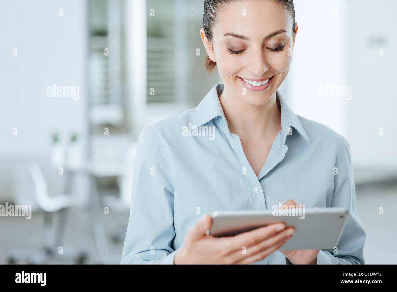 Young smiling business woman en utilisant un écran tactile numérique et utiliser des applications, il est debout dans le bureau Banque D'Images