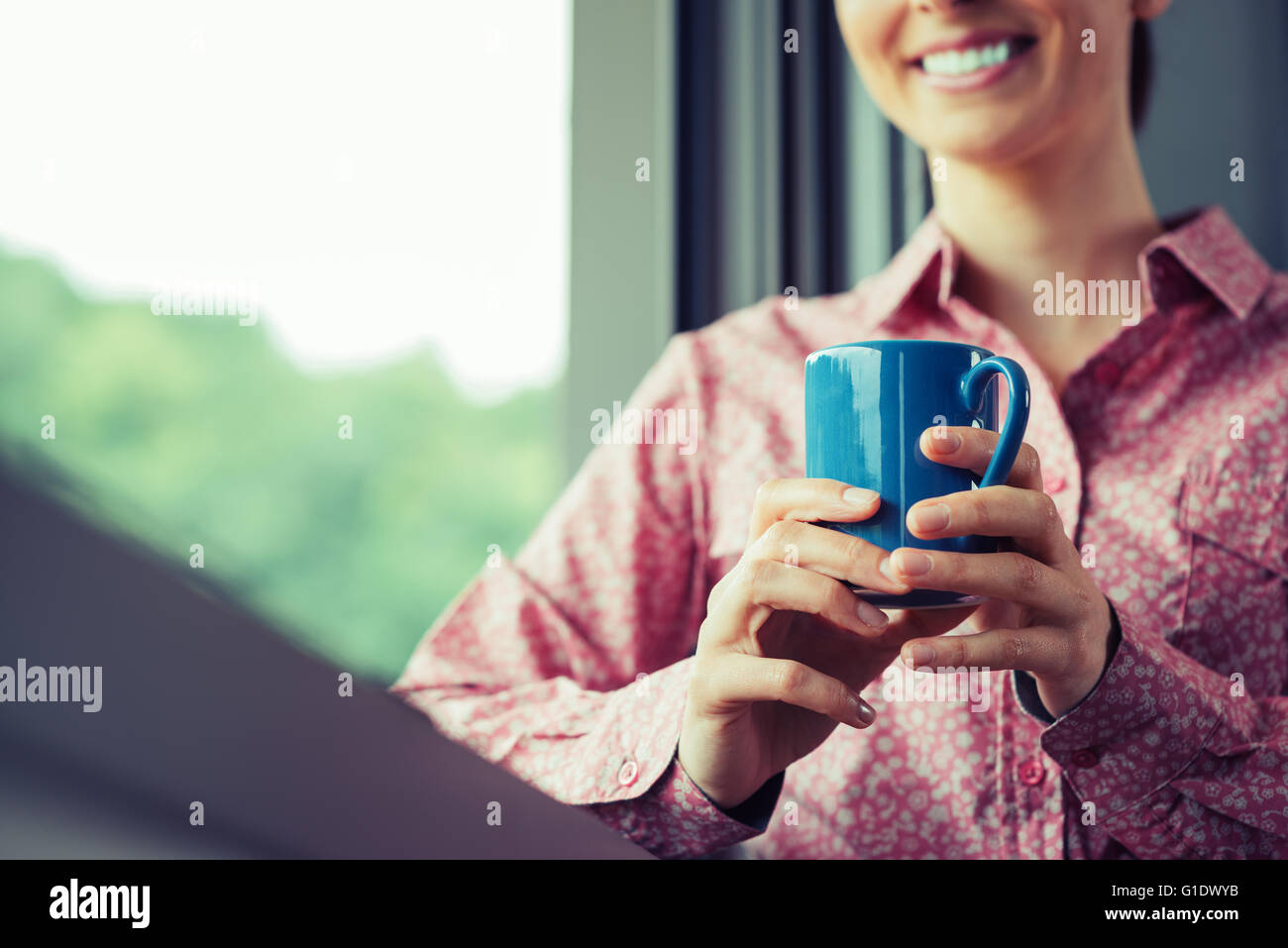 Femme ayant une pause café à fenêtre, elle est souriante et tenant une chope Banque D'Images