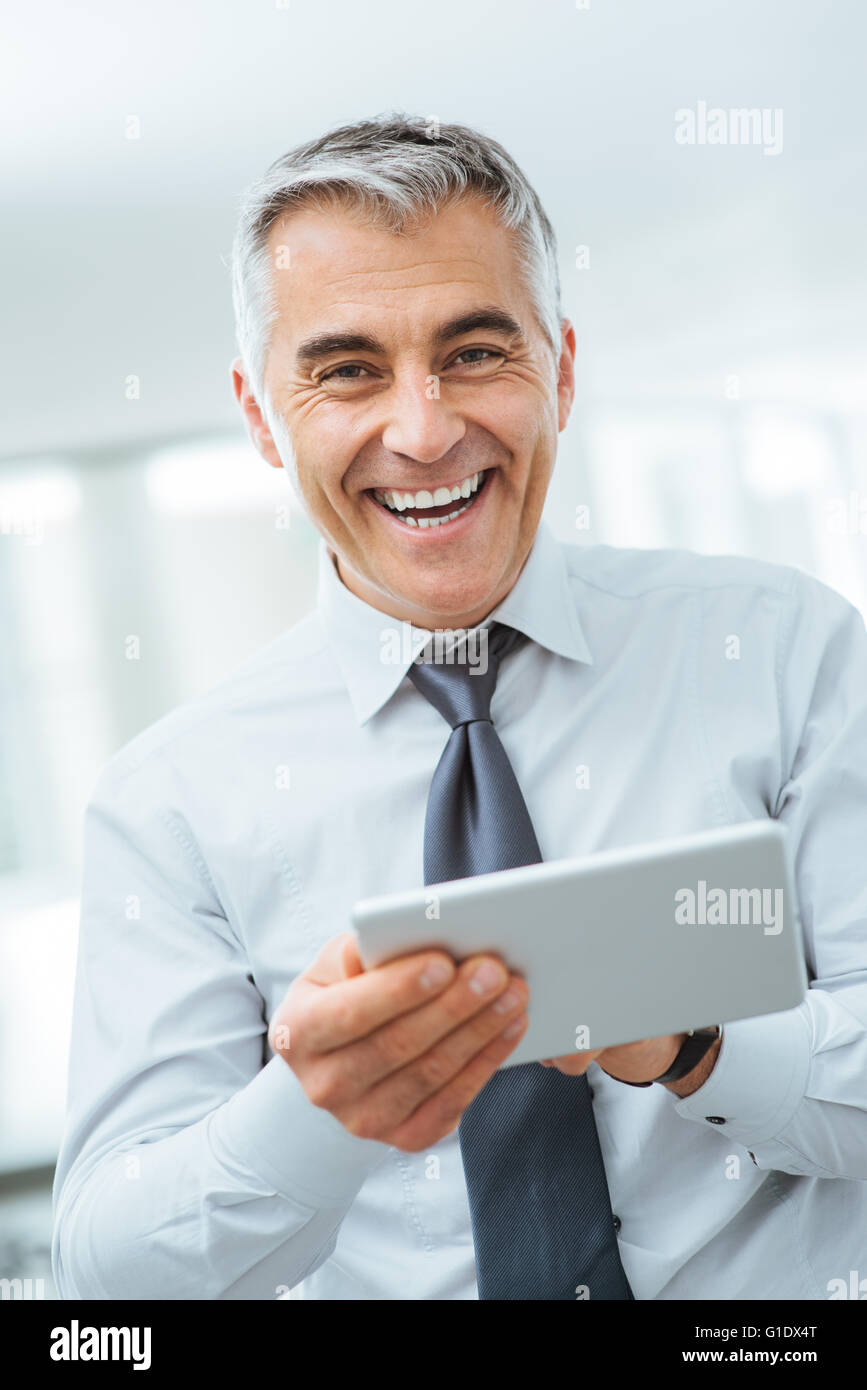 Smiling confident businessman looking at camera et à l'aide d'un écran tactile numérique Banque D'Images