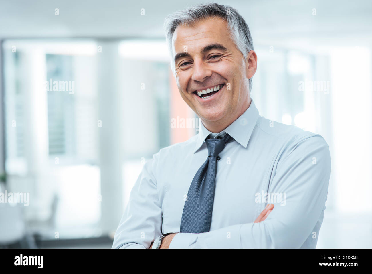 Les businessman posing with crossed arms and smiling at camera Banque D'Images