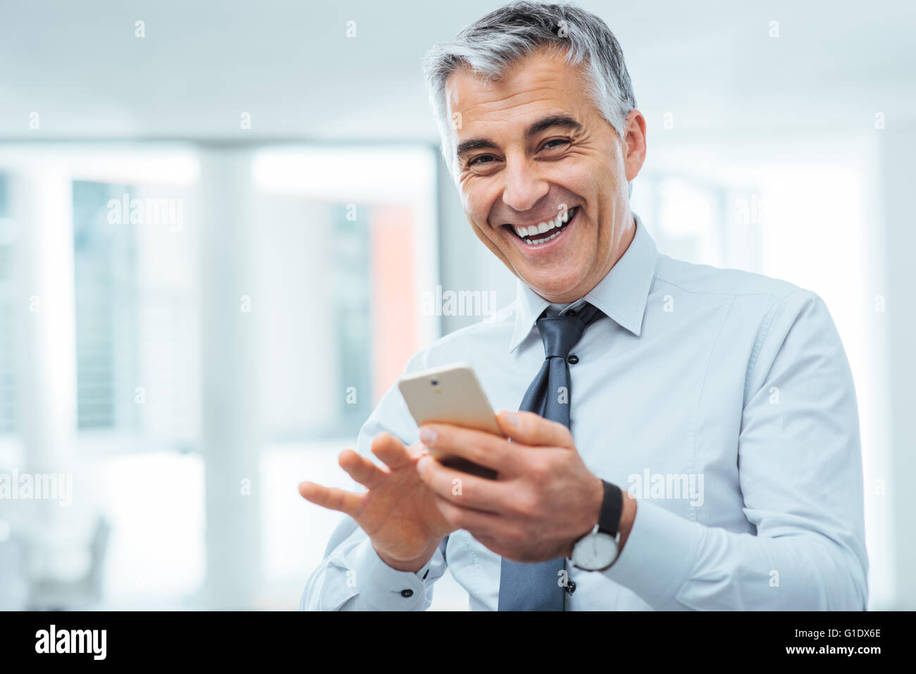 Cheerful businessman Smiling en utilisant un écran tactile smart phone and looking at camera Banque D'Images