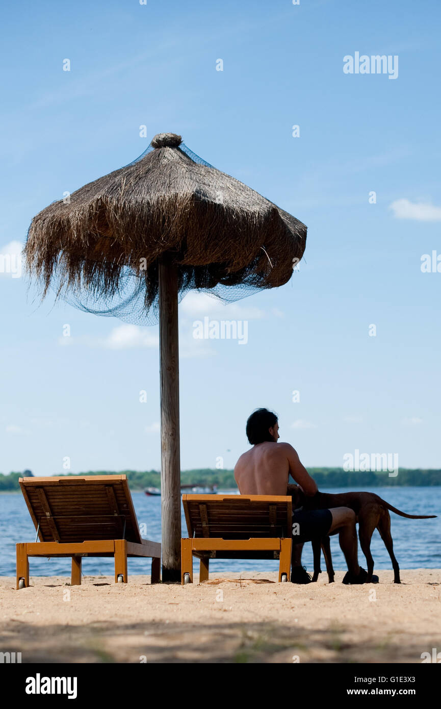 Petzow, Allemagne. 13 mai, 2016. ILLUSTRATION - Un homme est assis sur une chaise de plage avec son chien à côté de lui à l'Caputh lido et donne sur le lac Schwielowsee de Petzow, Allemagne, 13 mai 2016. La qualité de l'eau de tous les 251 lacs de baignade est excellente selon le ministère de l'consommateurs de Brandebourg. Photo : Klaus-Dietmar Gabbert/dpa/Alamy Live News Banque D'Images