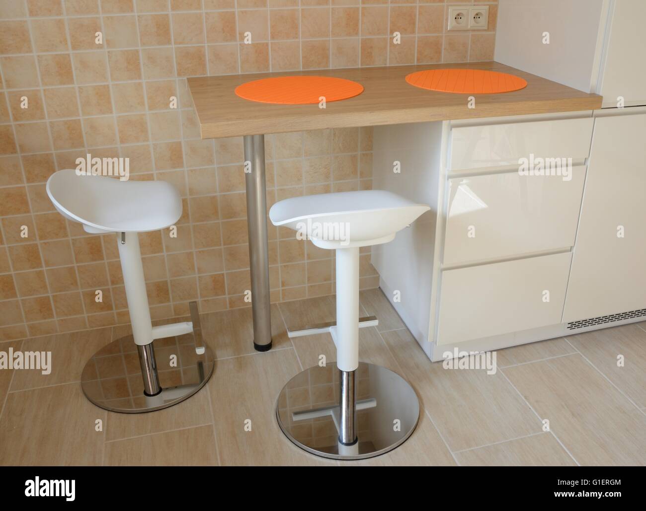 Deux tabourets pivotants et petite table de cuisine avec table en caoutchouc orange au mur recouvert de tuiles Banque D'Images