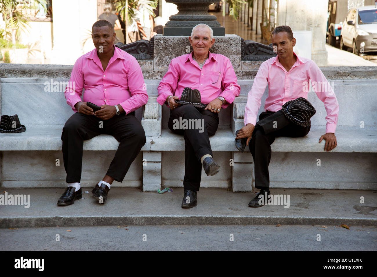 Trois mâles chanteurs cubains vêtue de rose shirts et chapeaux de cow-boy s'asseoir sur un banc dans Centro Habana Cuba Banque D'Images