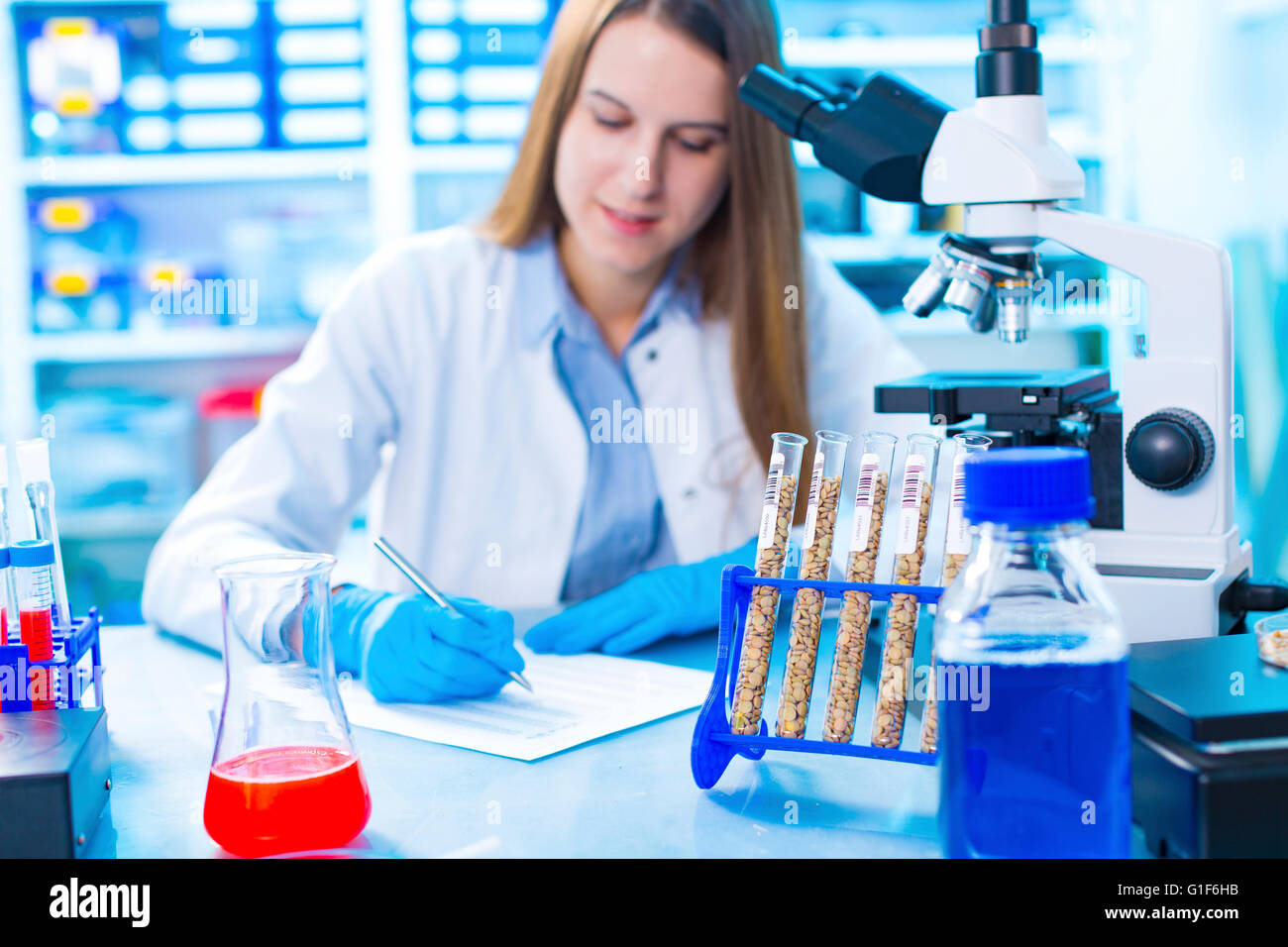 Parution du modèle. Technicien de laboratoire femelle la rédaction de notes, tubes à essai avec les légumineuses en premier plan. Banque D'Images