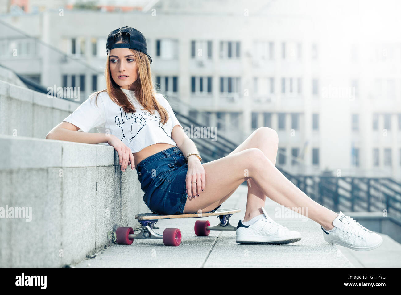 Jeune femme assise sur longboard dans le paysage urbain Banque D'Images