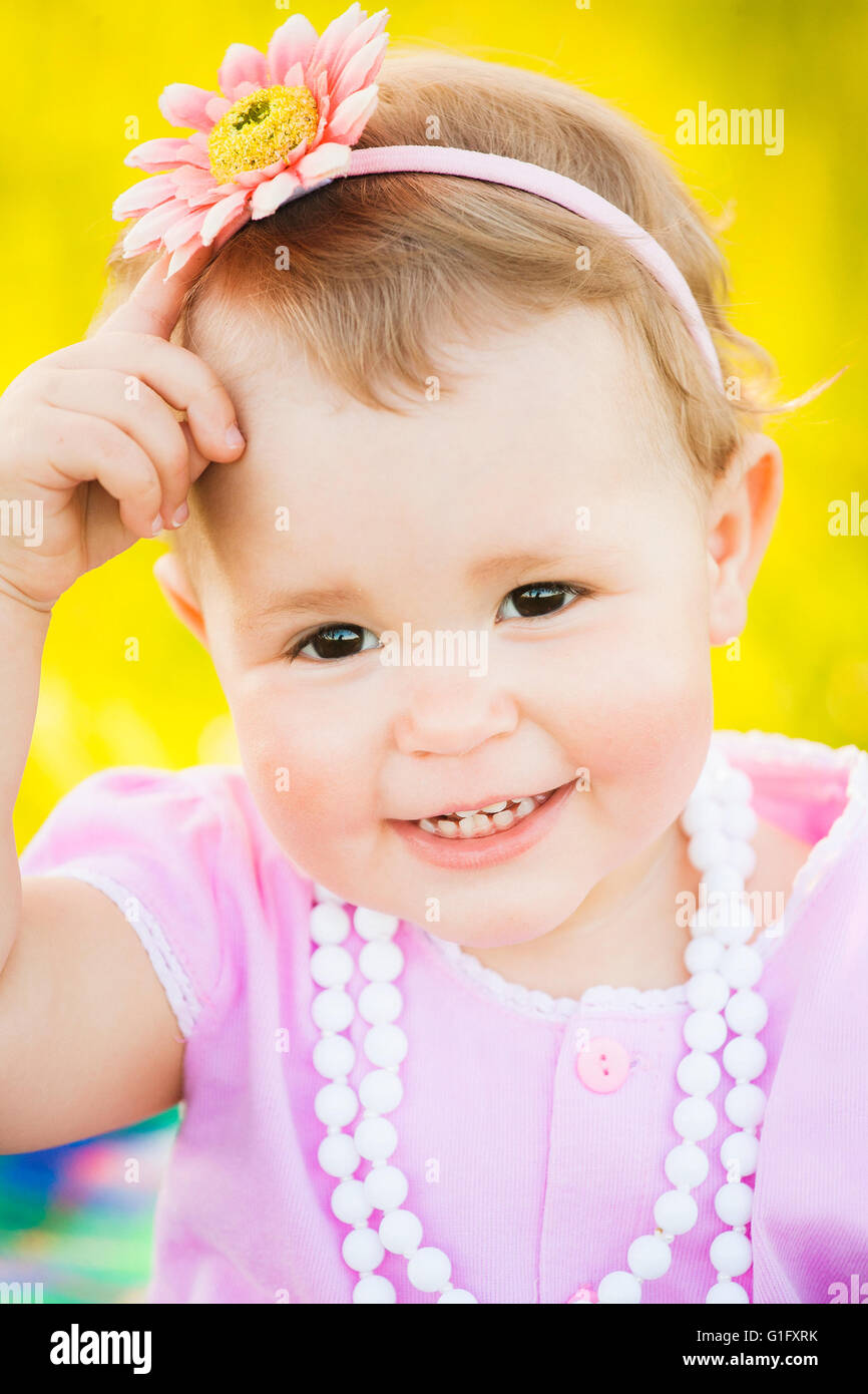 Close up portrait of charmant sourire d'un an petite fille habillé en robe rose mignon, collier blanc et rose fleur Banque D'Images