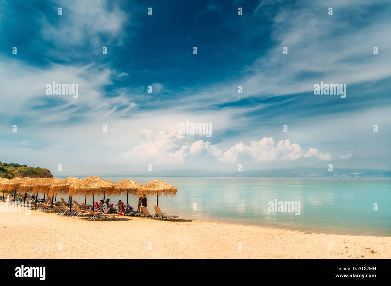 Parapluie de chaume, chaises longues sur une plage grecque et nuages reflets dans les eaux turquoise de la mer Égée, Nea-Fokea, Halkidiki Banque D'Images