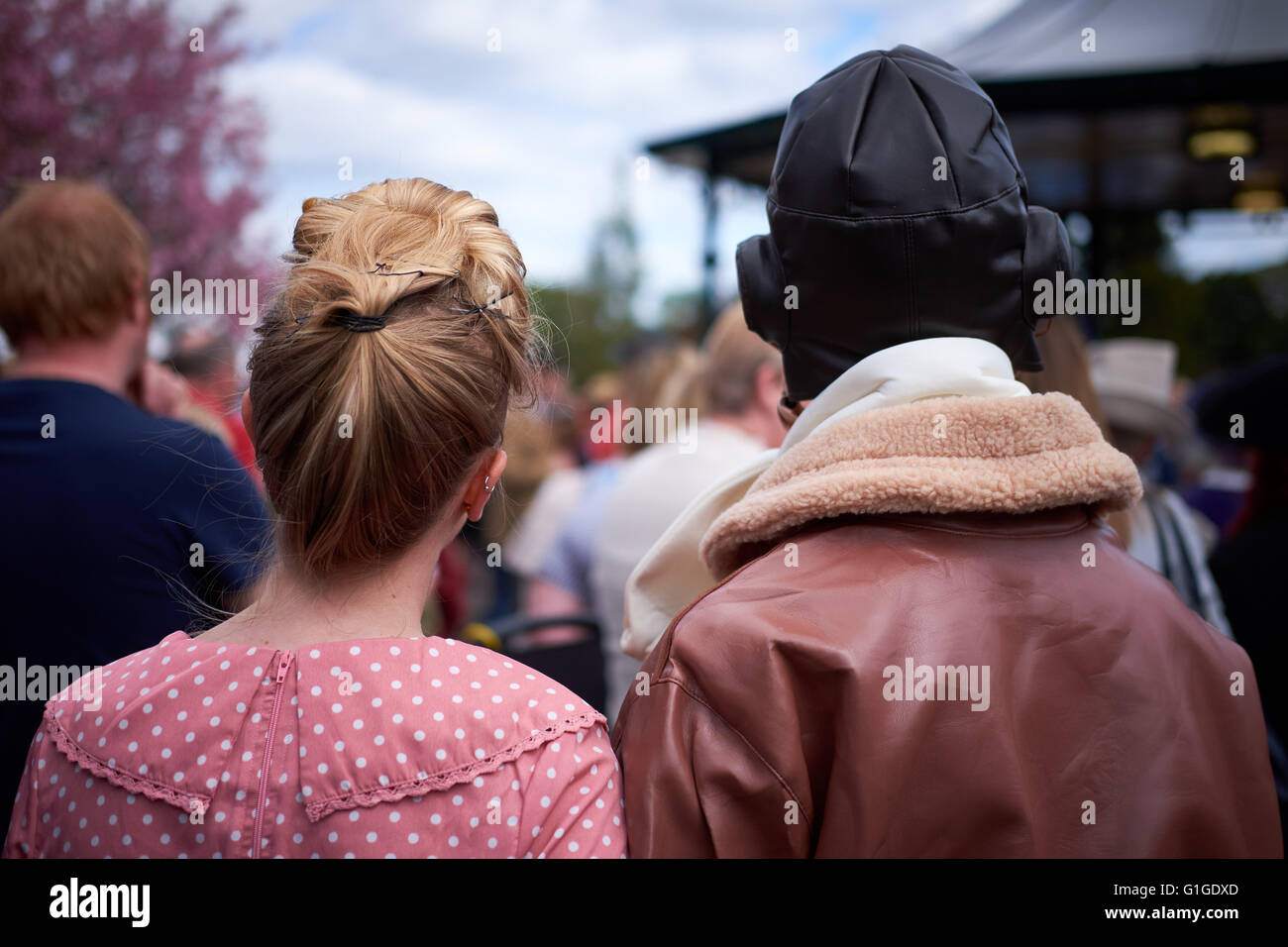 Un jeune couple, vêtu de vêtements vintage des années 40 et tiré par derrière, regarder un événement dans un kiosque à musique. Banque D'Images