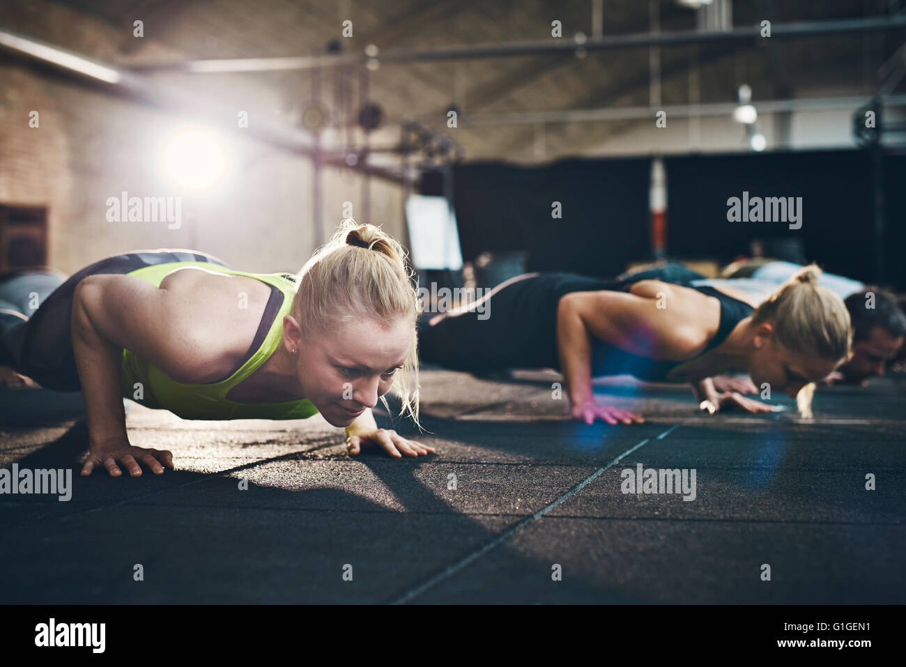 Fit young woman doing pushups à l'accent, s'entraîner dans un gymnase avec d'autres personnes Banque D'Images