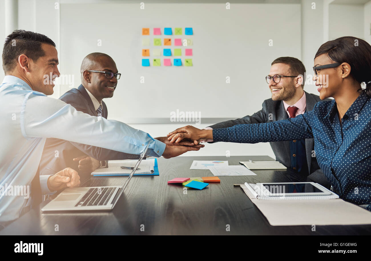 L'équipe entreprise multiraciale signalant leur engagement à l'autre par l'atteinte de l'autre côté de la table dans le bureau d'empiler les mains aussi Banque D'Images